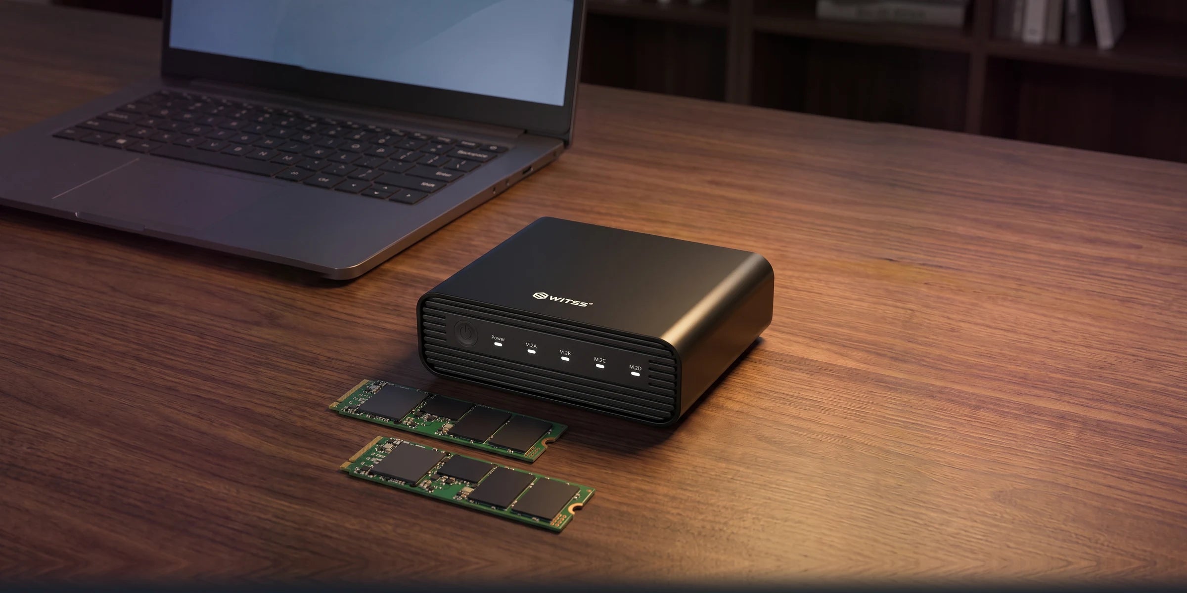 Le boîtier M.2 4 baies Switss sur un bureau en bois, avec deux SSD M.2 NVMe nus devant lui et un ordinateur portable en arrière-plan
