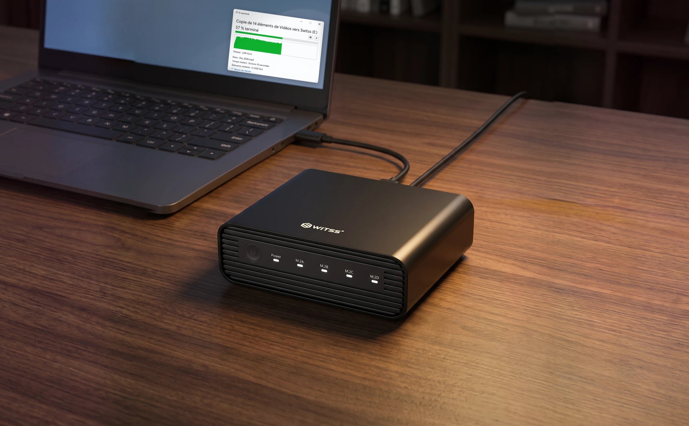 Le boîtier M.2 4 baies Switss relié à un ordinateur portable par le câble USB-C, câble d’alimentation branché, avec une copie de fichiers vers le disque en cours à l’écran