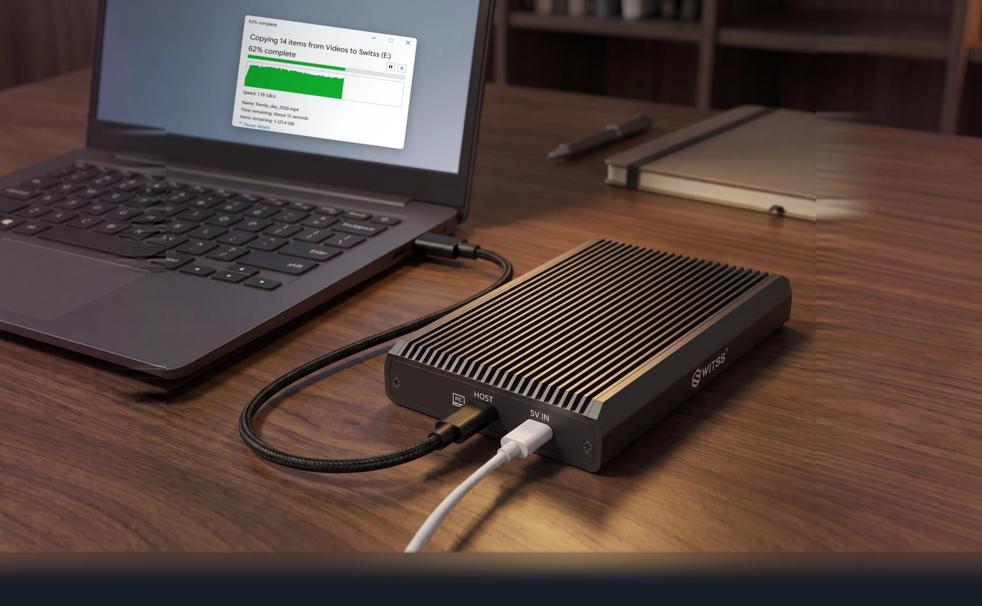 Switss® RAID dual-bay enclosure on a walnut desk, cable running to a laptop with a copy window open