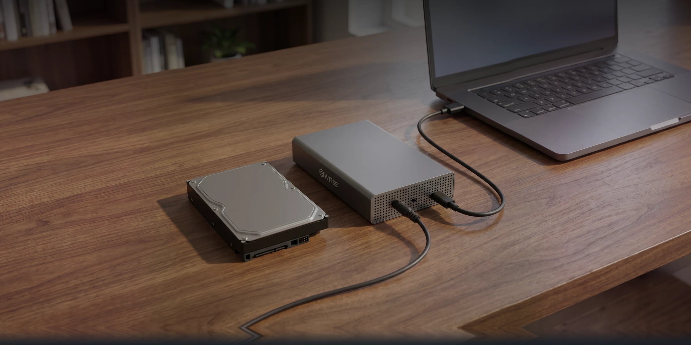 The Switss 3.5 inch enclosure on a wooden desk next to a bare hard drive, with the USB cable running to a laptop and the power adapter connected