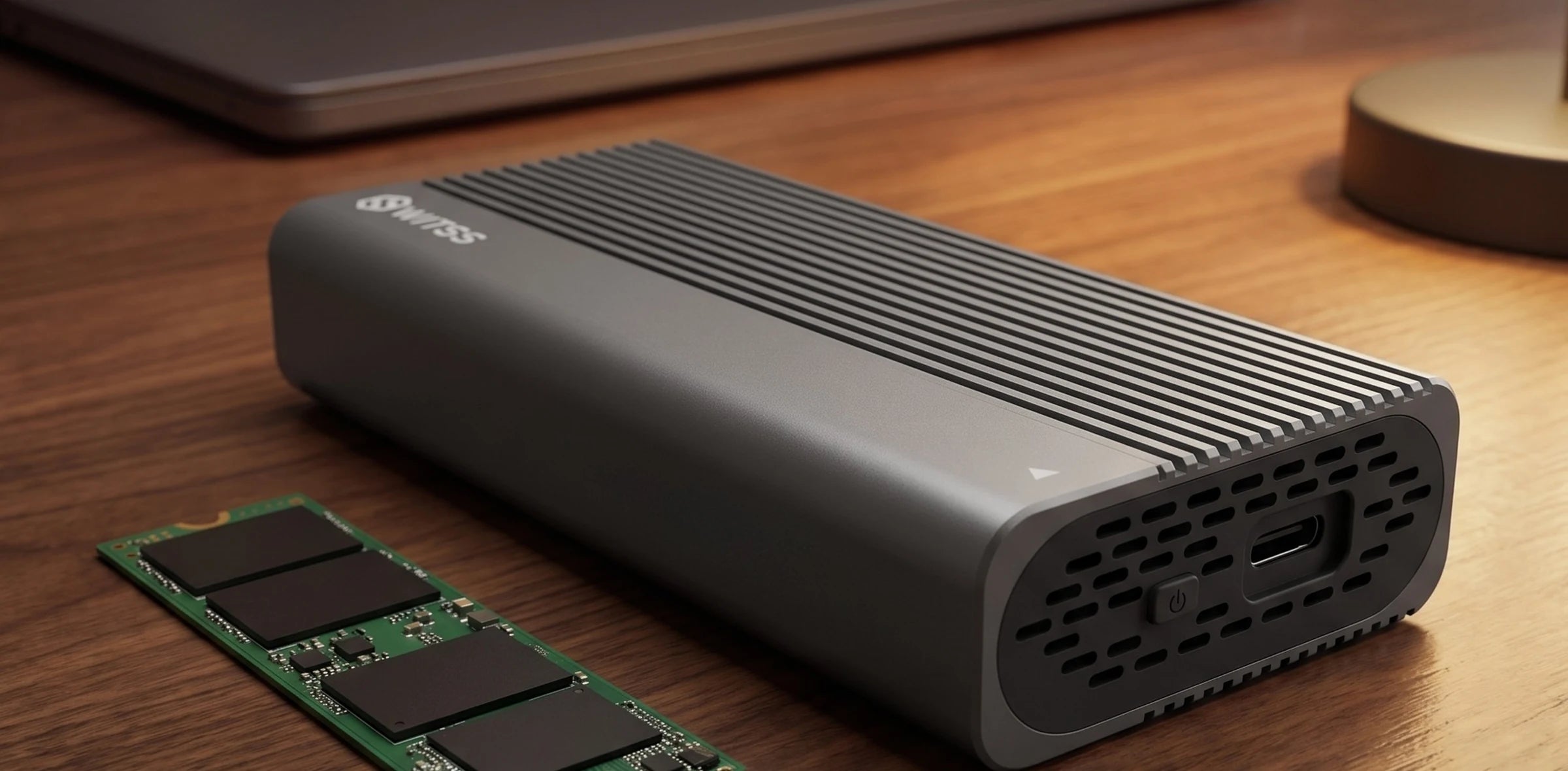 Le boîtier M.2 Switss sur un bureau en bois, avec un SSD M.2 NVMe nu à côté et un ordinateur portable fermé en arrière-plan