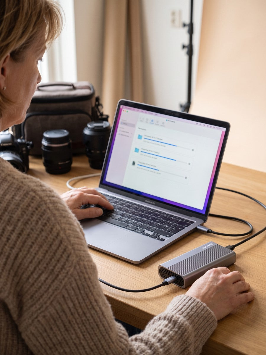 A woman transfers video files, laptop with a progress list and a camera on the table